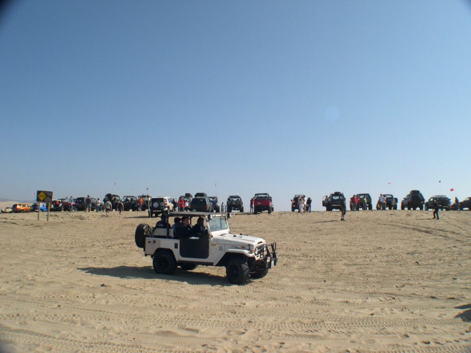 White open-top Toyota FJ40 driving on sand dunes with 4x4s lined up behind