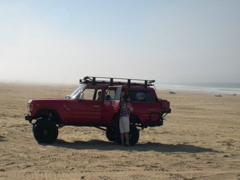 2007 Toyota FJ Cruiser - Red Toyota Land Cruiser FJ60 parked on a sandy beach with the ocean in the background.