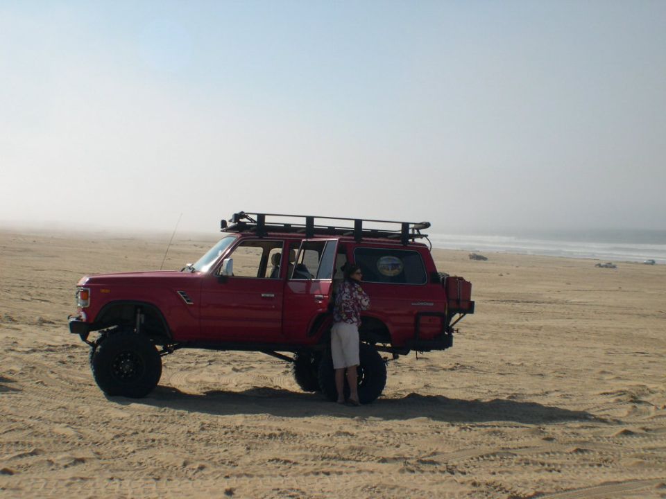 Lifted red Toyota Land Cruiser wagon with roof rack parked side-on at the beach