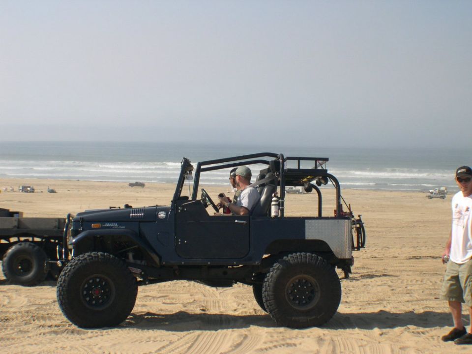 Dark blue open-top Toyota Land Cruiser FJ40 with roll cage parked on a beach