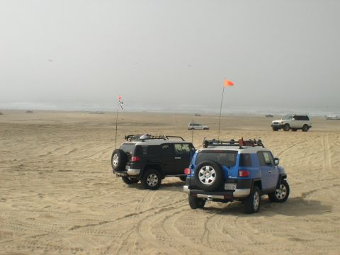 2007 Toyota FJ Cruiser - Two Toyota FJ Cruisers are parked on a sandy beach near the ocean, with flags attached to their antennas.