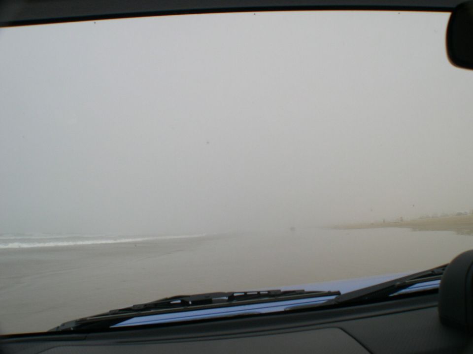View through a 4x4 windshield driving on a foggy beach with surf breaking to the left