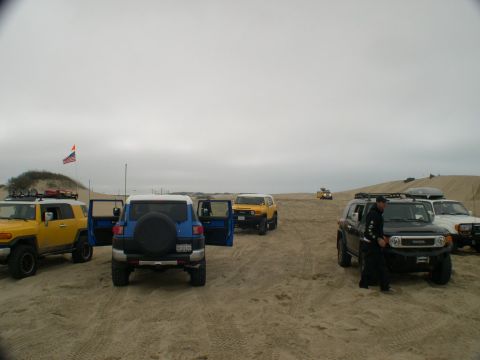 2007 Toyota FJ Cruiser - A group of Toyota FJ Cruisers are gathered on a sandy landscape, with an American flag visible in the background.