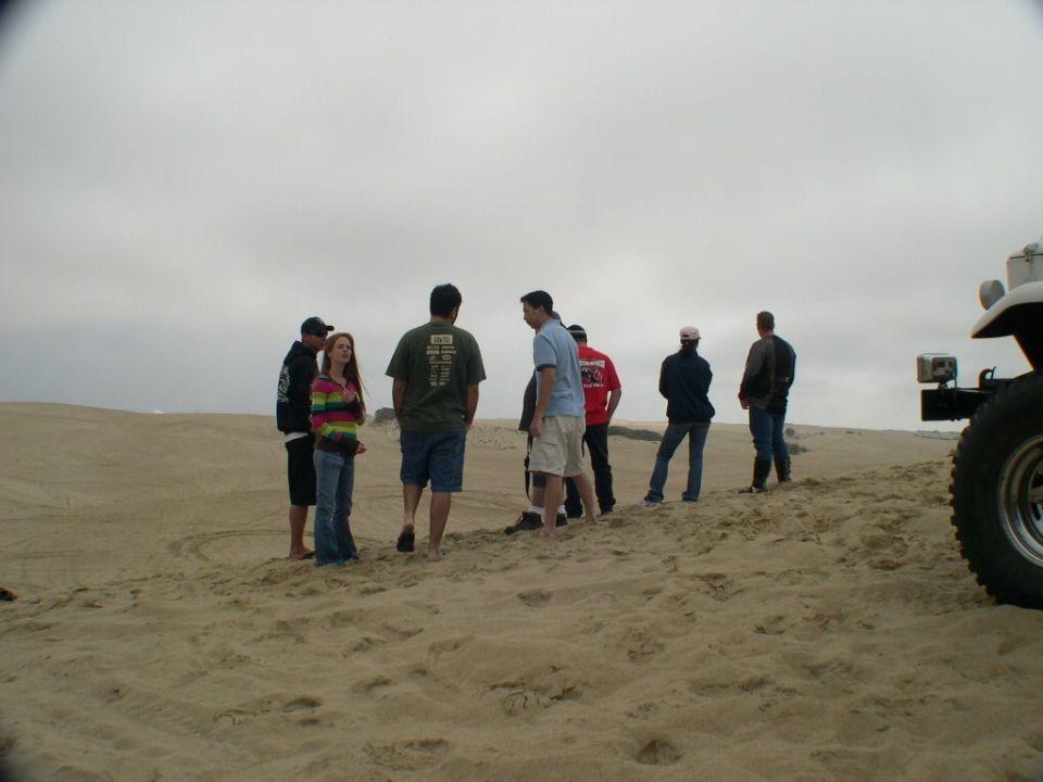 People standing on a sand dune beside the front corner of a white 4x4 on knobby tires