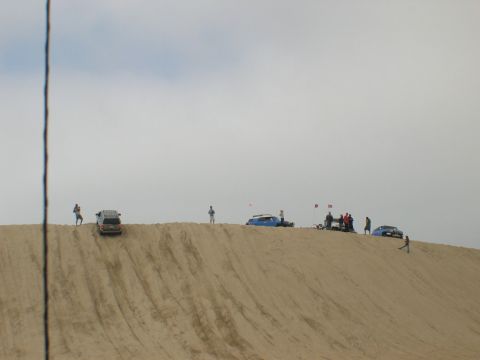 2007 Toyota FJ Cruiser - People and vehicles gathered on a sand dune on a cloudy day.