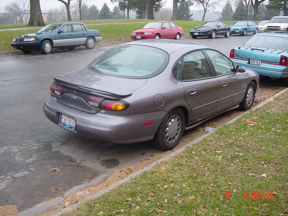Gray Ford Taurus parked on street, rear view. Other cars visible