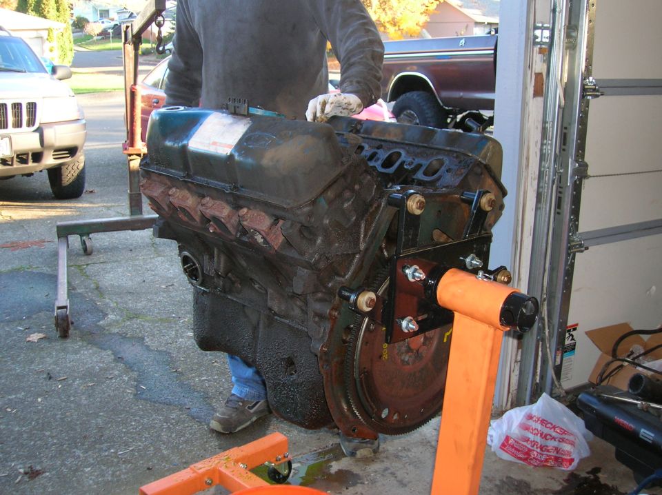 Engine on an orange engine stand, with a Jeep SUV and a pickup truck in the background