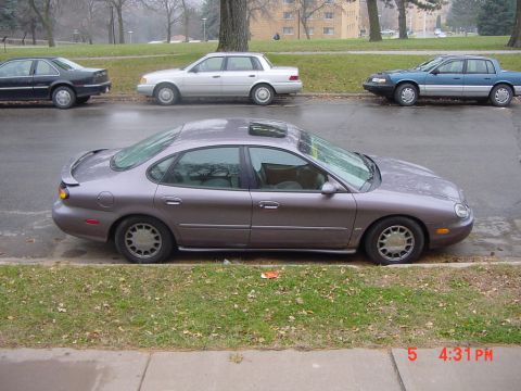 1996 Ford Taurus - A 1996 Ford Taurus is parked on the side of the road with other vehicles in the background.