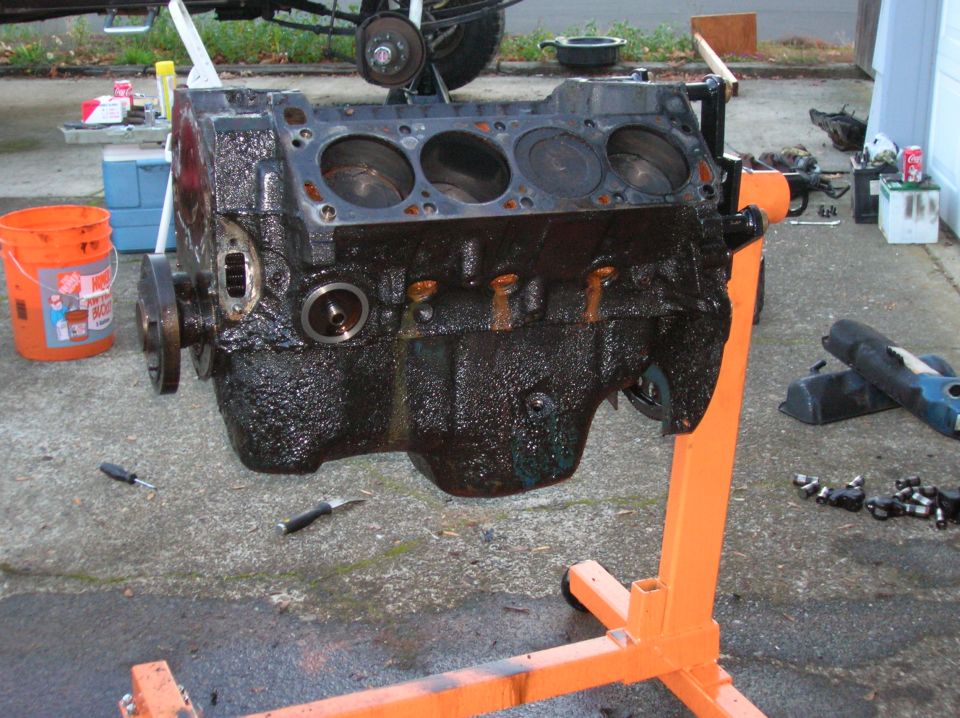 Engine block on an orange stand, looks greasy. Tools and buckets nearby
