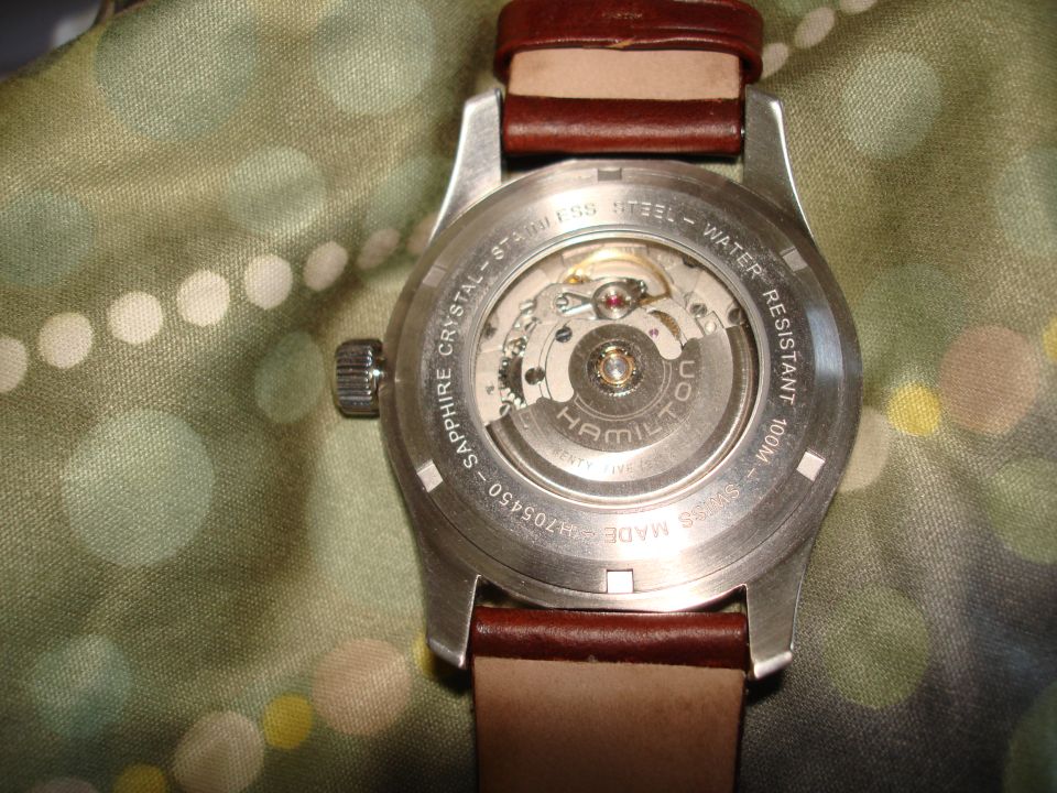 Watch caseback showing automatic movement and Hamilton branding. Brown leather strap visible