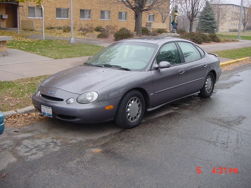 Gray 1996 Ford Taurus sedan parked on wet asphalt, front 3/4 view