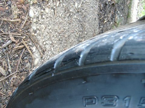1999 Ford Mustang - Close-up of a damaged tire, showing tread wear and sidewall cracks.