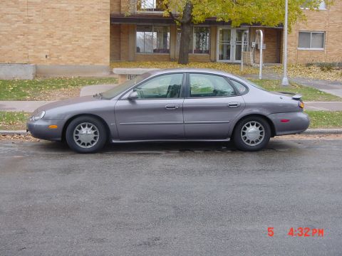 1996 Ford Taurus - A gray 1996 Ford Taurus is parked on the side of a street in front of a brick building.