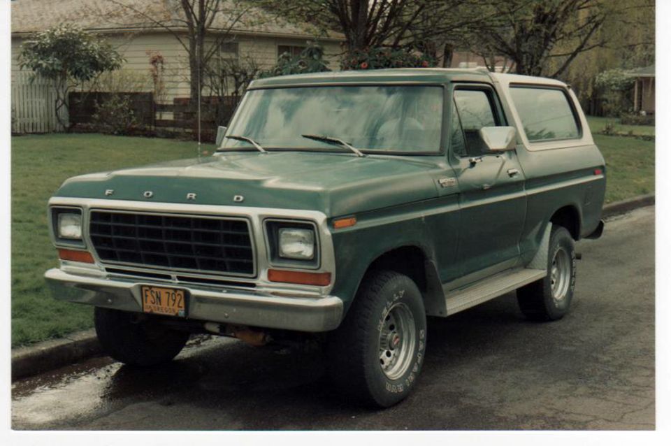 Green 1979 Ford Bronco with a white top, parked on a street