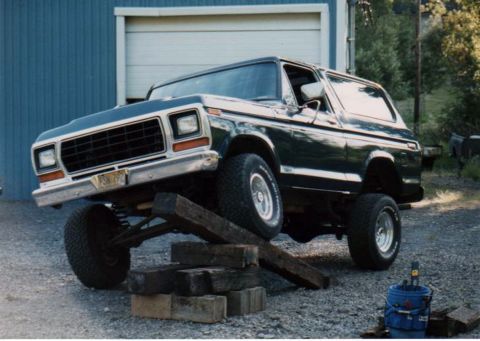 1979 Ford Bronco - A dark green Ford Bronco is positioned on wooden blocks, with its front driver side wheel raised off the ground.