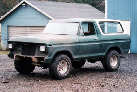 1979 Ford Bronco - A 1978 Ford Bronco in dark green and white sits on a gravel lot in front of a blue building.
