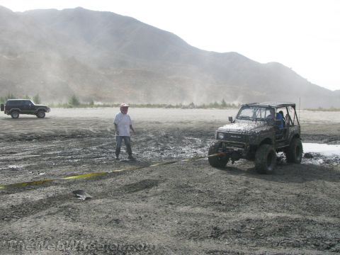1987 Suzuki Samurai - A Suzuki Samurai is being pulled out of the mud by another vehicle while a person watches.