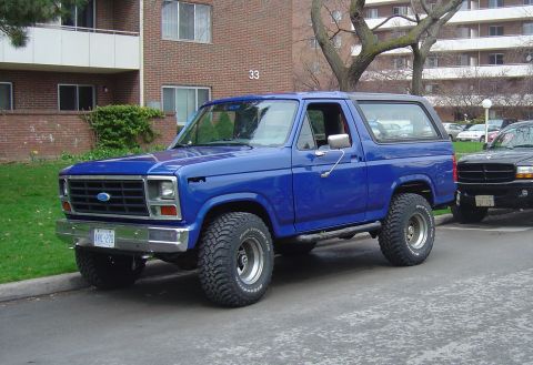 1986 Ford Bronco - This blue Ford Bronco is parked on a street in front of an apartment building.