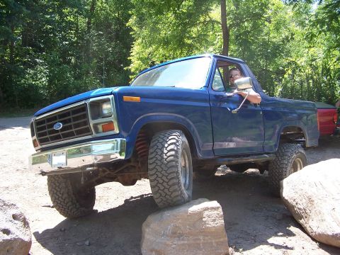 1986 Ford Bronco - This lifted blue Ford Bronco navigates a rocky trail, its off-road capabilities.