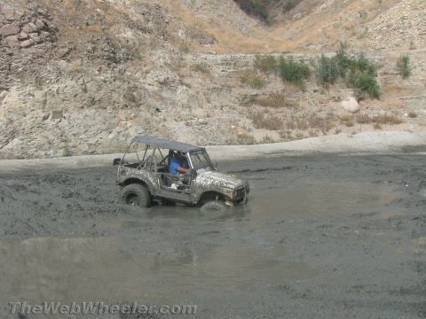 1987 Suzuki Samurai - A Suzuki Samurai navigates through a thick mud pit in a dry, rocky terrain.