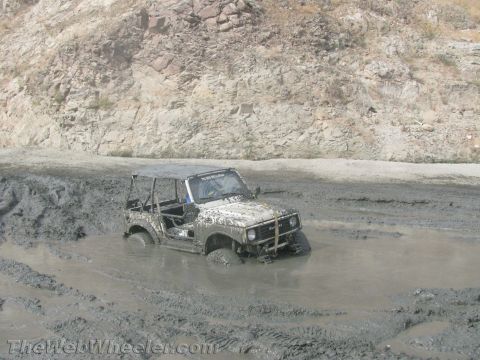 1987 Suzuki Samurai - A Suzuki Samurai is stuck deep in mud, its tires submerged and body splattered with dirt.