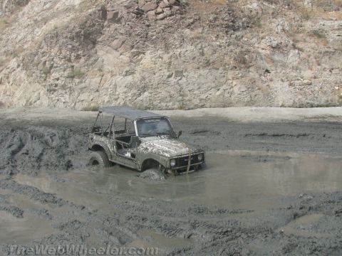 1987 Suzuki Samurai - A 1987 Suzuki Samurai is deeply stuck in thick mud, with only its top and front visible above the mire.