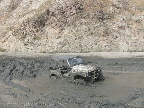 1987 Suzuki Samurai - A 1987 Suzuki Samurai is stuck deep in mud while off-roading near a rocky hillside.