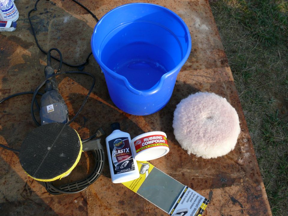 Car detailing supplies including a polisher, bucket, rubbing compound, and polishing pad on a rusty surface