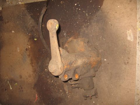 1979 Ford Bronco - A close-up of a weathered steering linkage part, likely from an older vehicle, resting on a stained concrete surface.