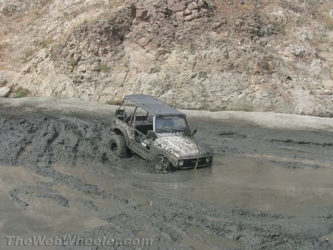 1987 Suzuki Samurai - A Suzuki Samurai is stuck deep in mud, with tire tracks visible in the muddy terrain.