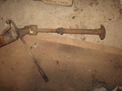 1979 Ford Bronco - This rusty driveshaft component is lying on a concrete floor next to some wooden planks.