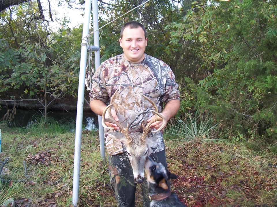 Man in camouflage holding a deer rack, with a dog nearby