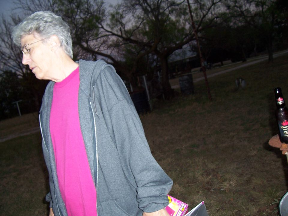 Person in a grey zip-up hoodie and pink t-shirt stands outdoors at dusk