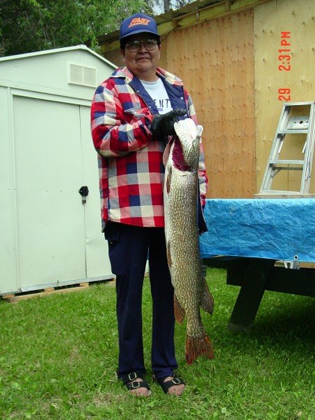 1990 Ford Bronco - A person proudly displays a large fish they caught, with a shed and wooden structure behind them.