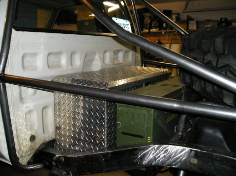 1986 Toyota Hilux - Diamond plate toolbox and green ammo cans are stored in the bed of a truck, secured by a roll cage.