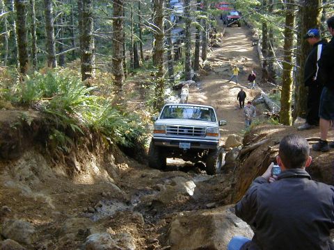 1994 Ford Explorer - White Ford Bronco tackling a challenging off-road course in a wooded area.