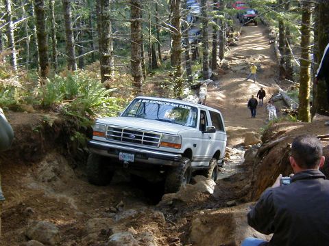 1994 Ford Explorer - A group of off-road vehicles tackle a challenging trail in a forest setting.