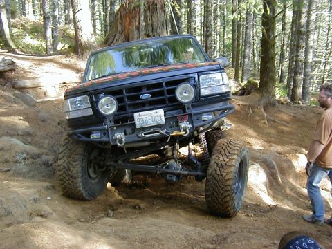 1994 Ford Explorer - This modified Ford Bronco is navigating a challenging off-road trail in a wooded area.