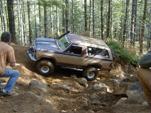 1994 Ford Explorer - A two-tone Ford Bronco navigates a challenging, rocky forest path during an off-road event.