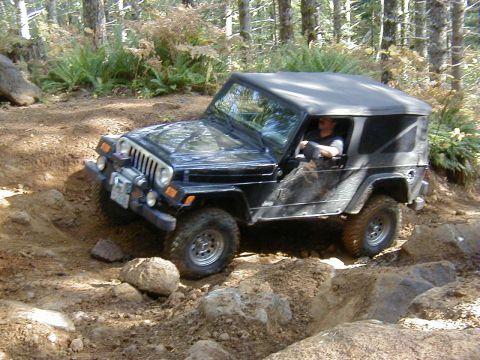 1994 Ford Explorer - Jeep Wrangler TJ tackling an off-road obstacle course in a forest setting.