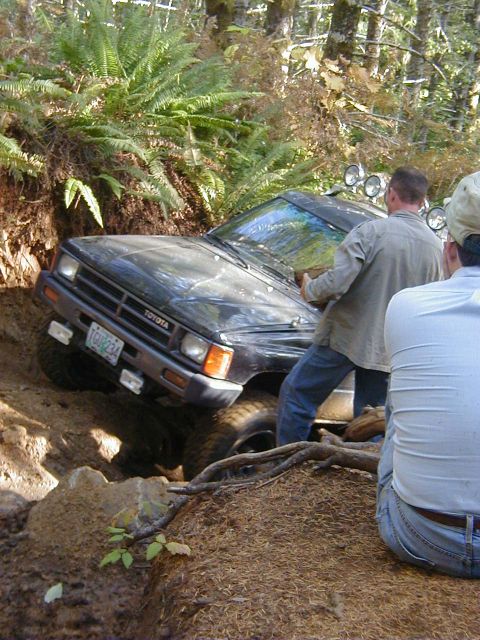 1994 Ford Explorer - A dark Toyota pickup truck is stuck in a muddy ditch with two people observing.