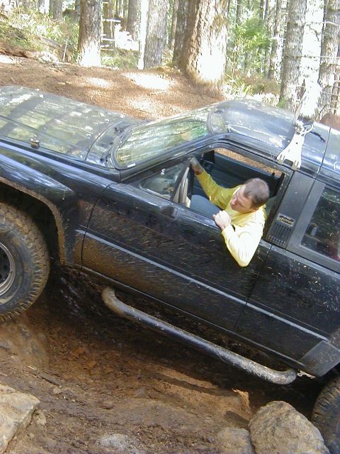 1994 Ford Explorer - Man drives a black SUV through a challenging off-road course with mud and rocks.