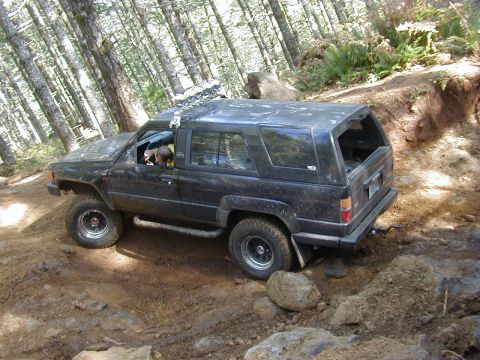 1994 Ford Explorer - A black Toyota 4Runner navigates a challenging off-road trail through a forest.