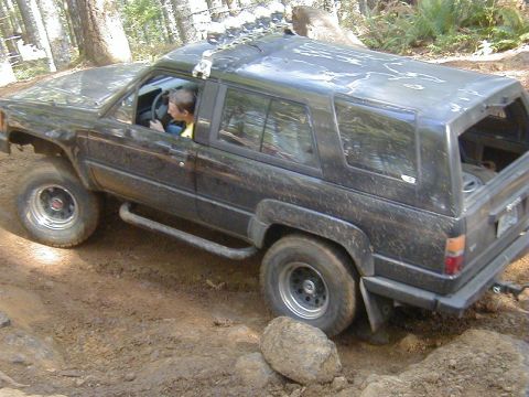 1994 Ford Explorer - A black SUV navigates a challenging off-road trail, its tires kicking up dirt and mud.