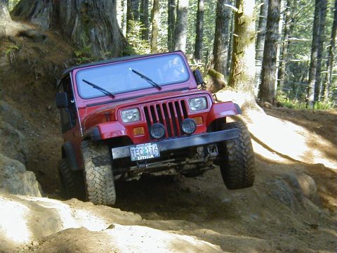 1994 Ford Explorer - A red Jeep Wrangler navigates a challenging off-road trail, with one wheel lifted.