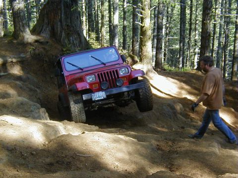 1994 Ford Explorer - A red Jeep Wrangler navigates a challenging off-road trail with steep inclines and rocky terrain.