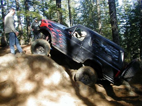 1994 Ford Explorer - A black SUV with flame decals navigates a steep, rocky incline during an off-road event.