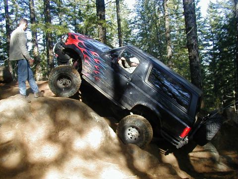 1994 Ford Explorer - A black SUV with custom flame decals navigates a challenging rocky terrain, demonstrating its off-road capabilities.