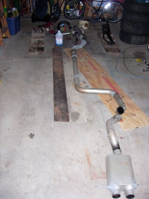 1994 Ford Probe - An exhaust system lies on a wooden plank on a garage floor, with various tools and parts scattered around.