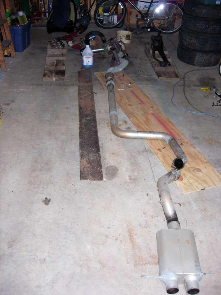 Exhaust system on a garage floor, with a bicycle and tires in the background